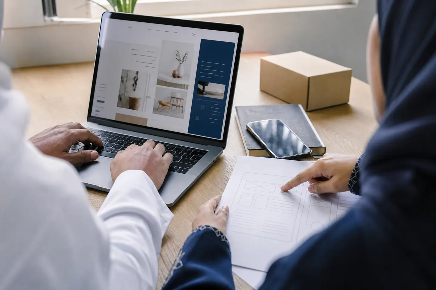يدان تراجعان مخطط واجهة ويب بجوار حاسوب محمول